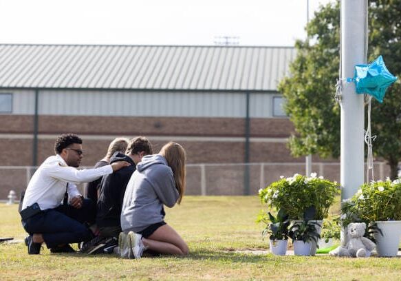 WINDER, GEORGIA - SEPTEMBER 5: State of Georgia Chaplain Ronald Clark consoles students as they kneel in front of a makeshift memorial at Apalachee High School on September 5, 2024 in Winder, Georgia. Two students and two teachers were shot and killed at the school on September 4, and a 14-year-old suspect, who is a student at the school, is in custody. (Photo by Jessica McGowan/Getty Images)